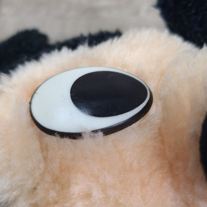 May include: Close-up of a plush toy's eye. The eye is black with a white crescent shape around it.