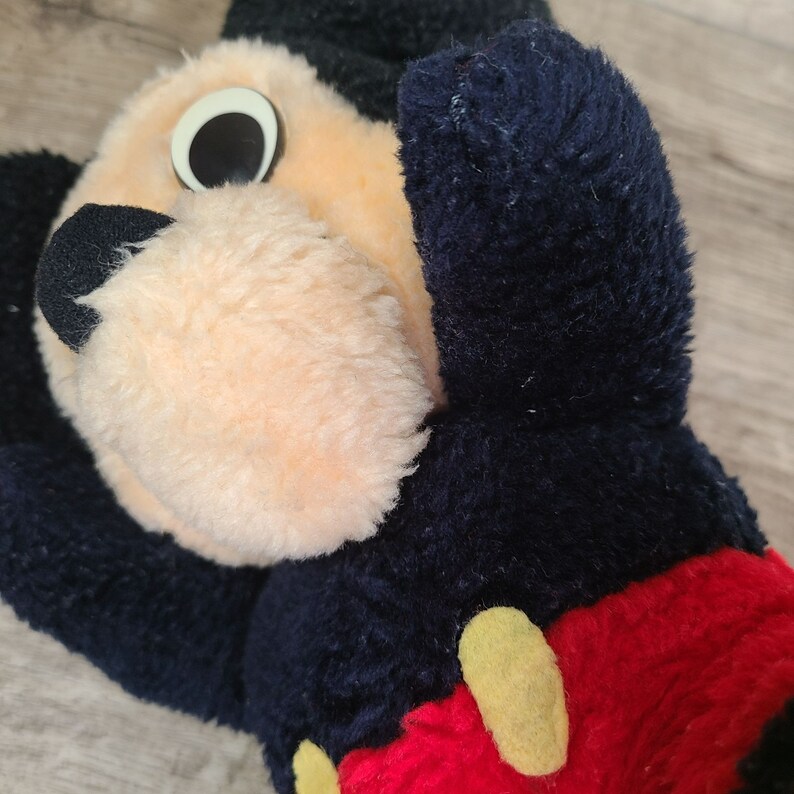 May include: A black and red plush Mickey Mouse toy with large black eyes and a yellow button on his red shorts.