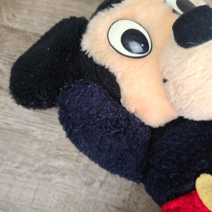 May include: A plush black and tan Mickey Mouse toy with large black eyes and a black nose. The toy is made of soft, fuzzy fabric.