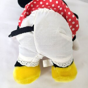 Pu&ograve; includere: Un giocattolo di peluche a forma di topo dei cartoni animati che indossa un vestito rosso e bianco a pois con un sottogonna bianco e scarpe gialle.