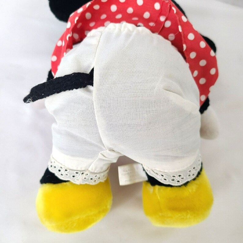 Pu&ograve; includere: Un giocattolo di peluche a forma di topo dei cartoni animati che indossa un vestito rosso e bianco a pois con un sottogonna bianco e scarpe gialle.