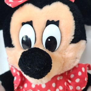 Pu&ograve; includere: Un giocattolo di peluche a forma di topo dei cartoni animati che indossa un vestito rosso con pois bianchi. Il topo ha grandi occhi neri e un naso nero.