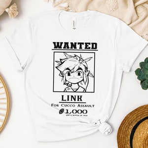 Puede incluir: Una camiseta blanca con un gráfico en blanco y negro de un cartel de búsqueda con Link de la serie de videojuegos The Legend of Zelda. El cartel dice "WANTED LINK FOR CUCCO ASSAULT 1,000 AND A BOTTLE OF MILK".