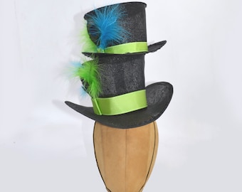May include: Two black top hats with green and blue feathers. The hats are stacked on top of each other and have green satin bands.