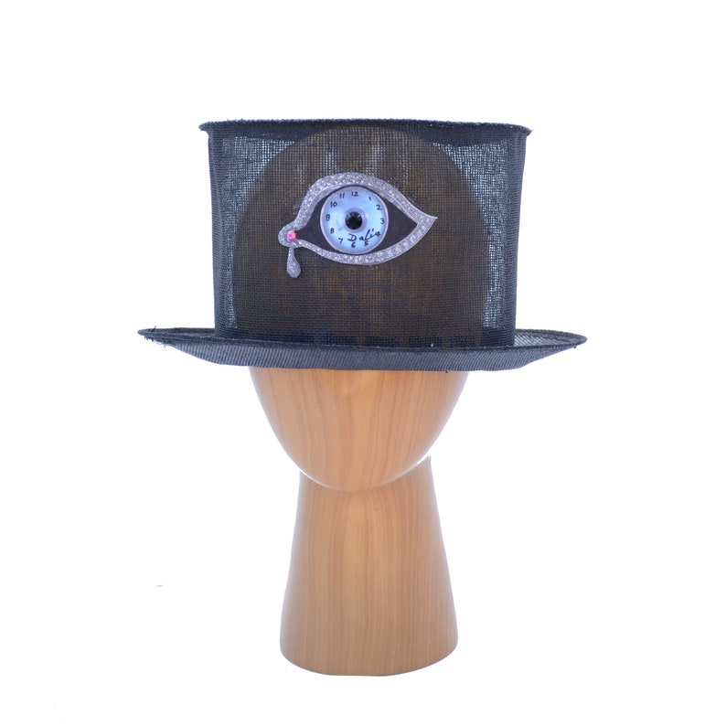 May include: A black top hat with a mesh fabric crown and a silver eye clock design. The eye has a blue face and a pink jewel.