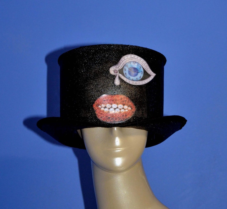 May include: A black top hat with a whimsical design featuring a blue eye with a clock face, a red mouth with white teeth, and a white teardrop.