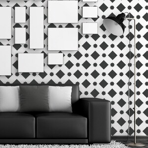 May include: A black leather sofa with three white and gray pillows in front of a white wall with a black and white geometric pattern. A black floor lamp with a black shade is in the corner of the room.