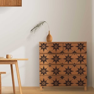 Puede incluir: Una cómoda de madera con cinco cajones presenta un patrón geométrico negro y marrón. El patrón está formado por formas de estrellas que se repiten.