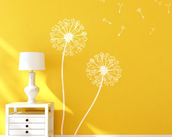May include: Two white dandelion decals on a yellow wall with a white lamp on a white nightstand. The dandelions are stylized and have seeds blowing in the wind.