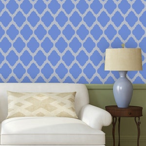 Puede incluir: Un sofá blanco con un cojín de estampado beige delante de una pared con estampado azul y blanco. Una lámpara azul con una pantalla beige se encuentra sobre una mesa auxiliar de madera.