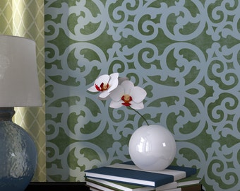 May include: A white ceramic vase containing a single stem of white orchids with red centres sits on a stack of four books. The vase is on a dark wood surface in front of a wall with a light blue and green patterned wallpaper.