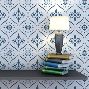 May include: A white lamp with a black base sits on a shelf with a stack of books. The shelf is against a white wall with a blue and white patterned wallpaper.