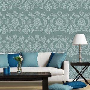 May include: A living room with a white sofa, blue cushions, and a dark wood coffee table. The teal wall features a damask pattern. A lamp is on a side table, and candles and a vase of flowers provide decoration.
