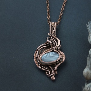 Peut inclure: Un pendentif en fil de cuivre enroulé avec une pierre d'agate grise et blanche. Le pendentif est suspendu à une chaîne en cuivre.