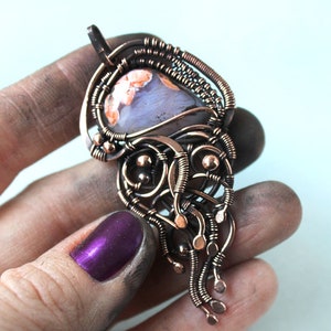 May include: A copper wire wrapped pendant featuring a light blue and orange agate stone. The pendant has a delicate, intricate design with copper wire loops and beads.