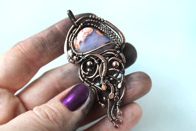 May include: A copper wire wrapped pendant featuring a light blue and orange agate stone. The pendant has a delicate, intricate design with copper wire loops and beads.