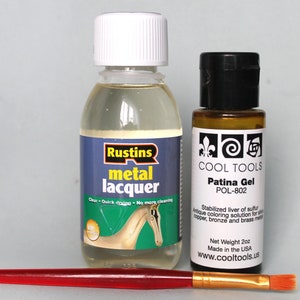 May include: Two bottles of metal finishing products. A clear bottle of Rustins metal lacquer and a brown bottle of Cool Tools Patina Gel. Both bottles are labeled with product information. A red and gold paintbrush is in the foreground.