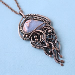 May include: A copper wire wrapped pendant necklace with a light blue and white agate stone. The pendant features a delicate, intricate design with a cascading effect.
