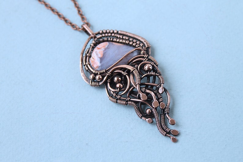 May include: A copper wire wrapped pendant necklace with a light blue and white agate stone. The pendant features a delicate, intricate design with a cascading effect.