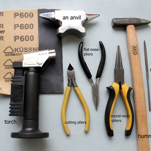 May include: A set of jewelry making tools including a torch, an anvil, a hammer, files, sandpaper, cutting pliers, flat-nose pliers, and round-nose pliers.