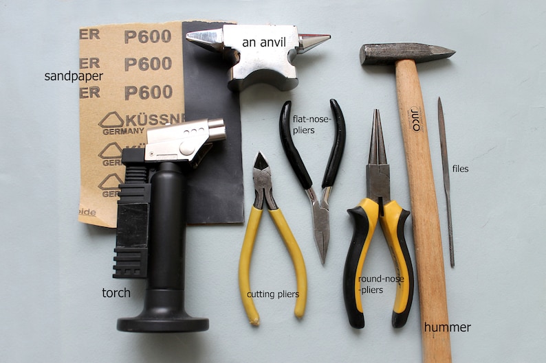 May include: A set of jewelry making tools including a torch, an anvil, a hammer, files, sandpaper, cutting pliers, flat-nose pliers, and round-nose pliers.