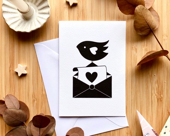 Black bird holding a letter, black and white greeting card. Cute bird card. A bird with a letter, envelope and love heart. A6 greeting card