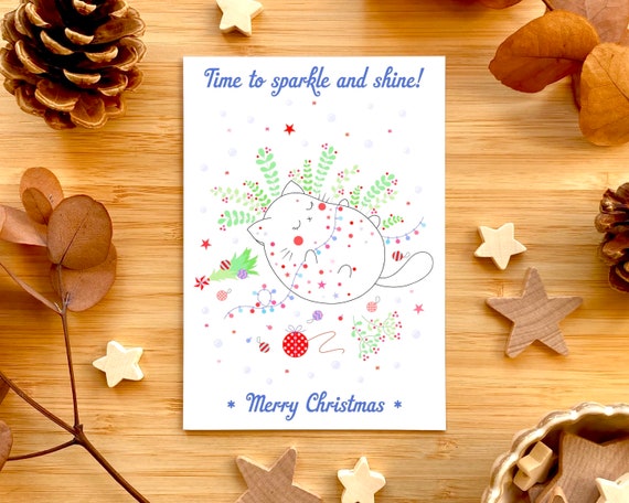 Time to sparkle and shine! Cute cat Christmas card. Cute cat playing with Christmas lights. Cat and Christmas tree.