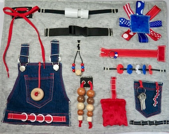May include: A busy board with various textures and activities for children. It features a denim overall with red stitching, a red zipper, a red and white ribbon, a wooden bead necklace, a red and white fabric square, a black buckle, a white plastic pipe, and a set of keys.