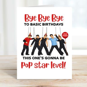 Puede incluir: Una tarjeta de cumpleaños blanca con el texto "Bye Bye Bye To Basic Birthdays" en rojo. La tarjeta presenta una caricatura de cinco hombres vestidos con varios atuendos, como si fueran marionetas. Un globo rojo con "Happy Birthday" es sostenido por uno de los hombres. El texto "This One's Gonna Be Pop Star Level!" también está en la tarjeta.
