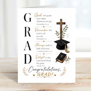 May include: A graduation greeting card with the word GRAD in large black letters. The card includes a cross, a graduation cap, and a small book. The text reads "God will guide your steps" and "Congratulations, GRAD!"