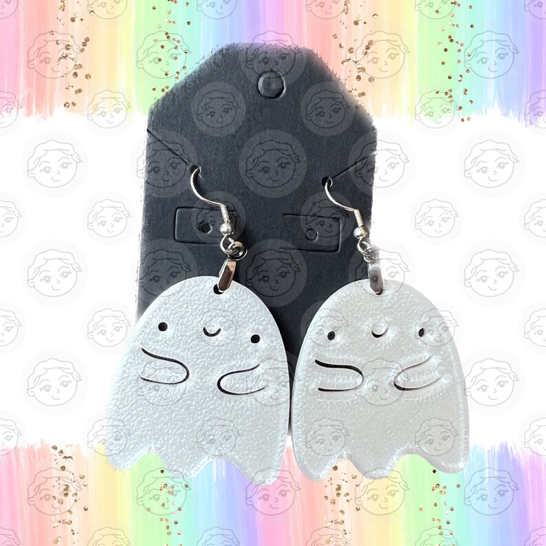 May include: A pair of silver ghost earrings with a smiling face and outstretched arms. The earrings are hanging from silver hooks.