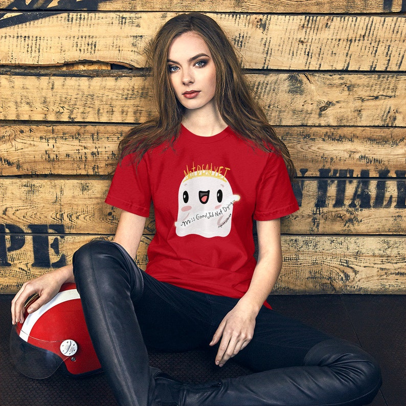May include: Red t-shirt with a white ghost wearing a gold crown and holding a wand. The ghost has a happy face and the text "This is Good, It Not Dream" is written on the shirt.