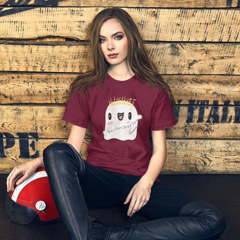 May include: A maroon t-shirt with a white ghost wearing a gold crown. The ghost has a smiling face and the text "Material Girl" above it and "This is Good, It's Not Drugs" below it.