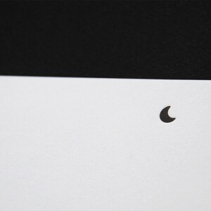 May include: A minimalist graphic design featuring a solid black horizontal band across the top half and a plain white lower half. A small, solid black crescent moon icon is positioned in the center of the white area, creating a stark contrast.