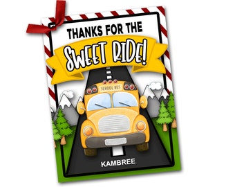 Puede incluir: Un autobús escolar amarillo con las palabras "School Bus" en el lateral, conduciendo por una carretera con montañas en el fondo. El autobús tiene una pancarta roja, blanca y amarilla encima que dice "¡Gracias por el dulce paseo!" y el nombre "Kambre" en la parte inferior.