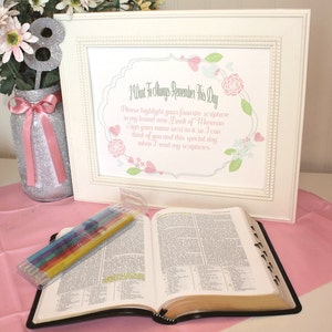 Könnte beinhalten: Ein weißer Rahmen mit einem Blumendesign und dem Text "I Want To Always Remember This Day" und "Please highlight your favorite scripture in my brand new Book of Mormon. Sign your name next to it so I can think of you and this special day when I read my scriptures." Eine schwarze Bibel liegt offen auf einer rosa Oberfläche, daneben ein Paket mit Buntstiften.