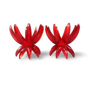 May include: Two translucent red acrylic stands, each featuring a multi-pronged, star-like design with curved, upward-reaching arms. These symmetrical objects have a hollow center and a wide base, constructed from smooth, glossy, vibrant red material.