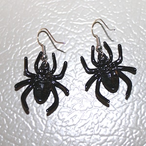 Peut inclure: Une paire de boucles d'oreilles en forme d'araignée noire avec des crochets argentés. Les araignées ont une finition brillante et lustrée.