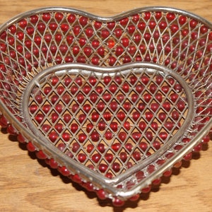 May include: A heart-shaped metal bowl with a wire mesh design. The bowl is decorated with red beads.