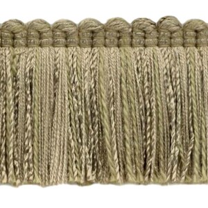 May include: A close-up of a beige fringe trim with a woven texture. The fringe is approximately 1 inch in length.