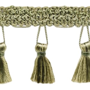 May include: A close-up of a gold fringe trim with tassels. The fringe is made of a woven fabric and has a subtle sheen. The tassels are approximately 2.5 cm long and are evenly spaced.