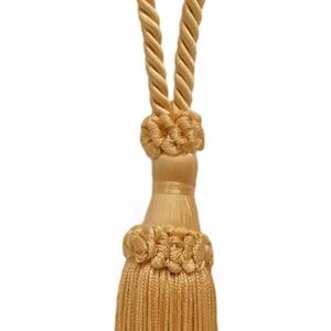 May include: A gold tassel tieback with a rope design. The tassel is made of a soft, silky material and has a long, flowing fringe.