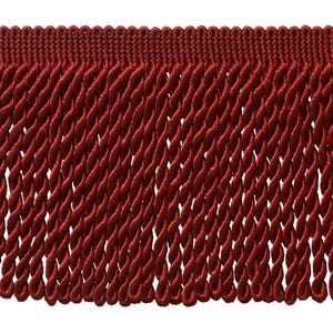 May include: Close-up of a burgundy-colored fringe trim. The trim features a woven top edge and a series of twisted rope-like strands hanging down. The fringe is densely packed, creating a textured and decorative element.