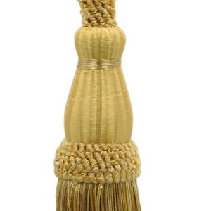 Può includere: Un fiocco dorato con una frangia e un nodo decorativo in cima. Il fiocco è fatto di un tessuto morbido e tessuto.