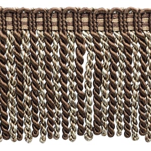May include: Close-up of decorative fringe trim in shades of brown and beige. The trim features a woven top section with a repeating pattern, and long, twisted rope-like strands hanging below. This trim is suitable for various craft and home decor projects.