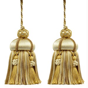 Peut inclure: Deux glands décoratifs aux tons or, crème et marron. Chaque gland présente un sommet bulbeux avec un motif en filet tissé, un corps satiné et une longue frange de fils dorés et crème. Suspendus par un cordon torsadé, pour la décoration.