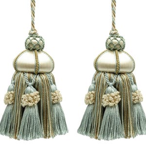 May include: Two decorative tassels in light blue, beige, and gold. Each has a bulbous top, a central woven section, and layered tassels. These tassels are likely for home decor, with a classic design and colour palette.
