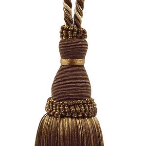 May include: A brown and gold tassel with a braided rope tie. The tassel is made of a soft, fluffy material and has a decorative knot at the top.