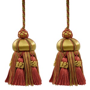 Puede incluir: Dos borlas decorativas con detalles dorados, rojos y verdes. Cada borla presenta una parte superior dorada en forma de cúpula con adornos rojos y verdes, una borla roja y un acento decorativo dorado. Las borlas cuelgan de un cordón trenzado.