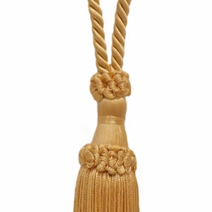 May include: A gold tassel tieback with a rope design. The tassel is made of a soft, silky material and has a long, flowing fringe.